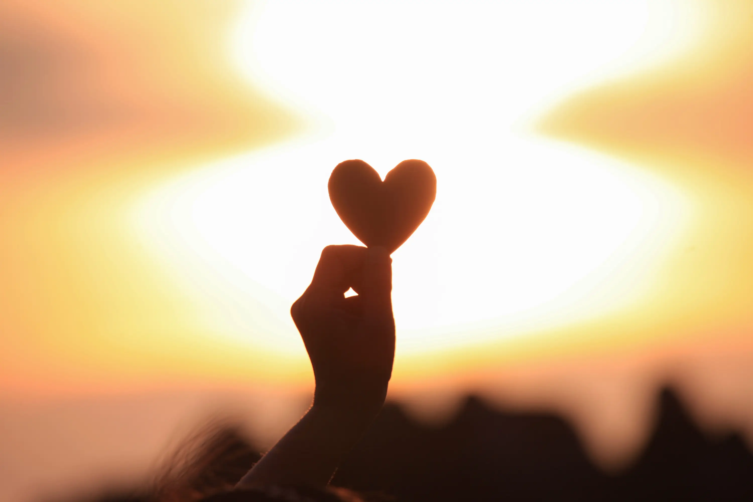 woman holding paper heart in hand up to sky